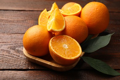 Photo of Fresh ripe oranges and leaves on wooden table, closeup