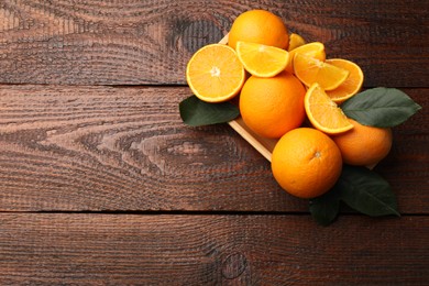 Photo of Fresh ripe oranges and leaves on wooden table, top view. Space for text