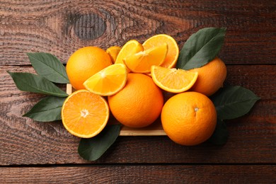 Photo of Fresh ripe oranges and leaves on wooden table, top view