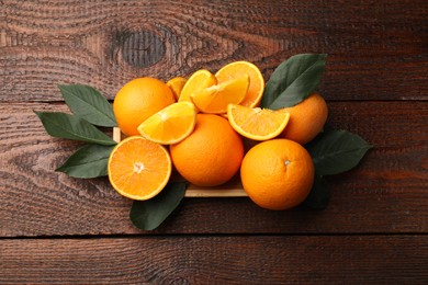 Photo of Fresh ripe oranges and leaves on wooden table, top view