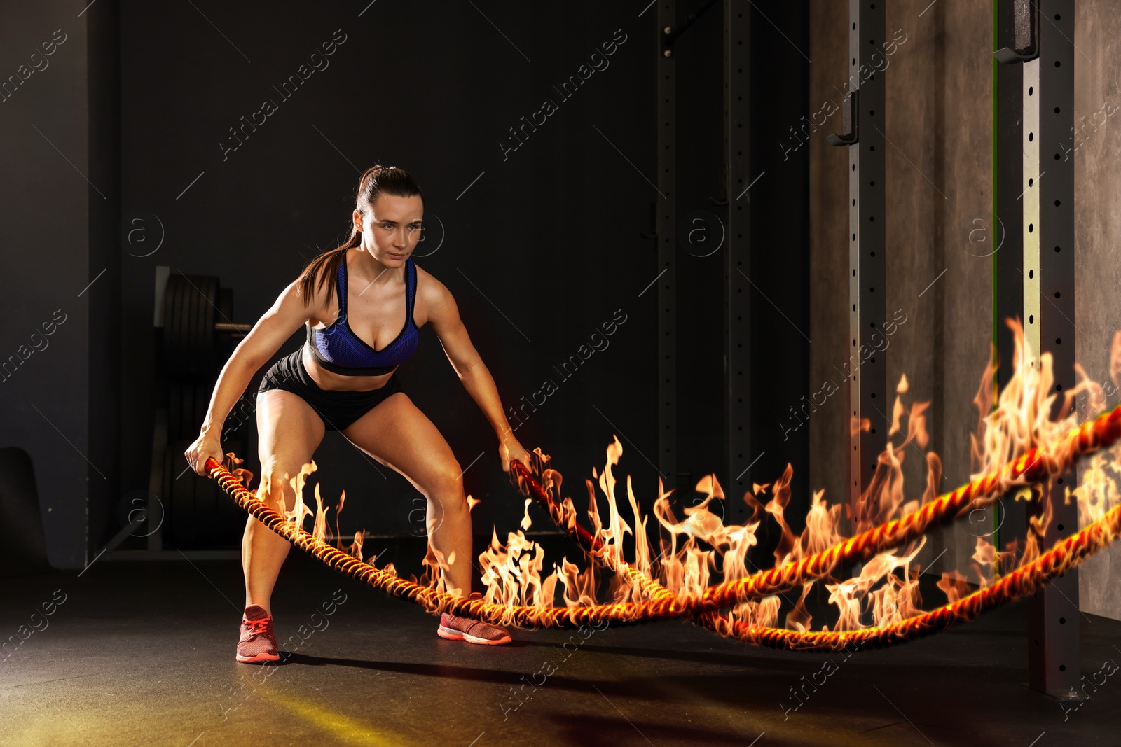 Image of Bodybuilding. Woman exercising with flaming battle ropes in gym