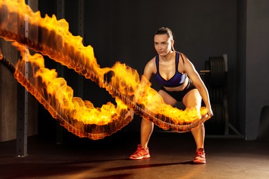 Image of Bodybuilding. Woman exercising with flaming battle ropes in gym