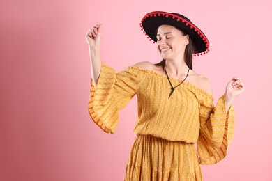 Photo of Smiling woman in black Flamenco hat and dress dancing on pink background. Space for text