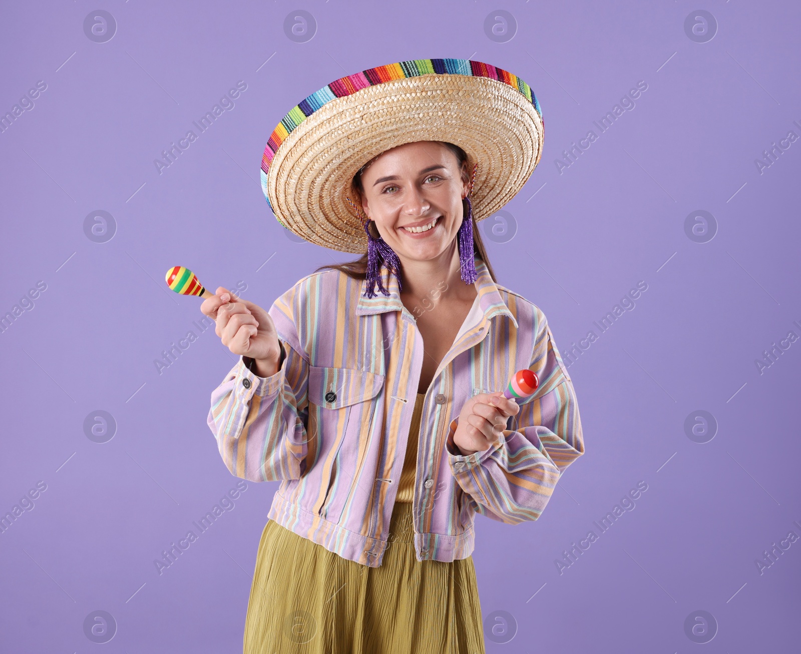 Smiling woman in sombrero hat playing maracas on violet background Photo of Smiling woman in sombrero hat playing maracas on violet background