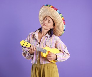 Photo of Woman in sombrero hat playing ukulele on violet background