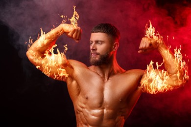 Image of Bodybuilder showing his biceps in smoke against dark background. Muscular man with flaming arms