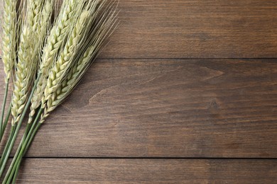Photo of Green wheat spikes on wooden table, flat lay. Space for text