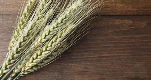 Photo of Green wheat spikes on wooden table, top view. Space for text