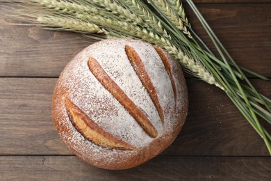 Photo of Fresh bread and green wheat spikes on wooden table, flat lay