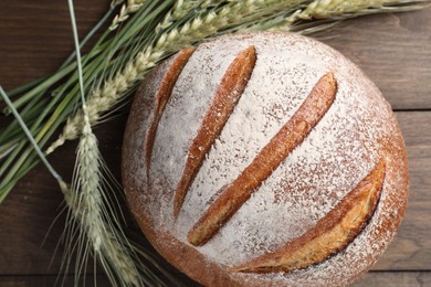 Photo of Fresh bread and green wheat spikes on wooden table, flat lay