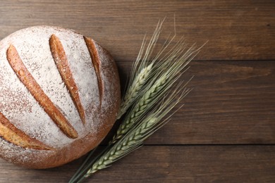 Photo of Fresh bread and green wheat spikes on wooden table, flat lay. Space for text