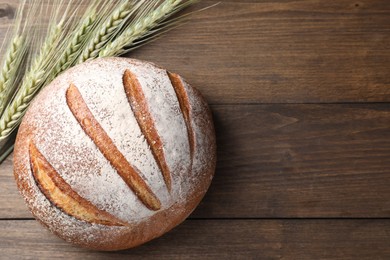 Photo of Fresh bread and green wheat spikes on wooden table, flat lay. Space for text