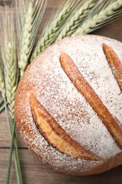 Photo of Fresh bread and green wheat spikes on wooden table, flat lay