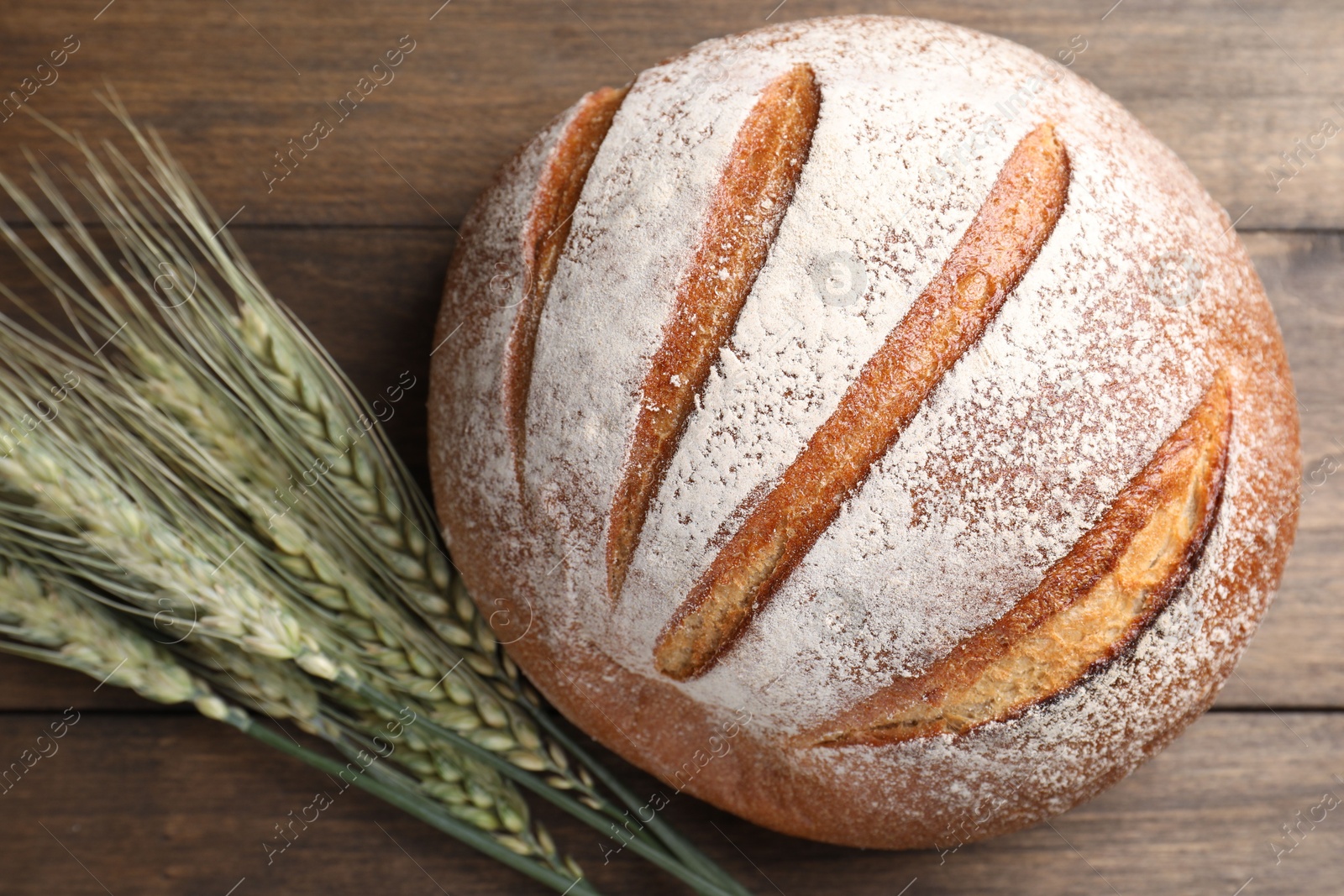 Photo of Fresh bread and green wheat spikes on wooden table, flat lay