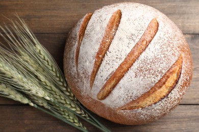 Photo of Fresh bread and green wheat spikes on wooden table, flat lay