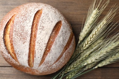Photo of Fresh bread and green wheat spikes on wooden table, flat lay