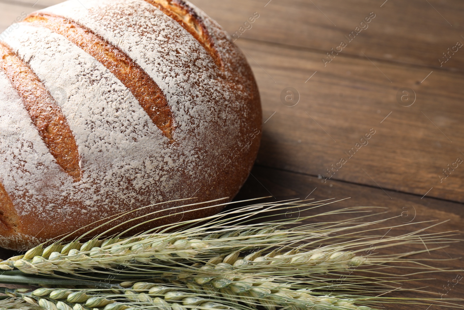 Photo of Fresh bread and green wheat spikes on wooden table, closeup. Space for text