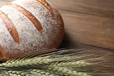 Photo of Fresh bread and green wheat spikes on wooden table, closeup. Space for text