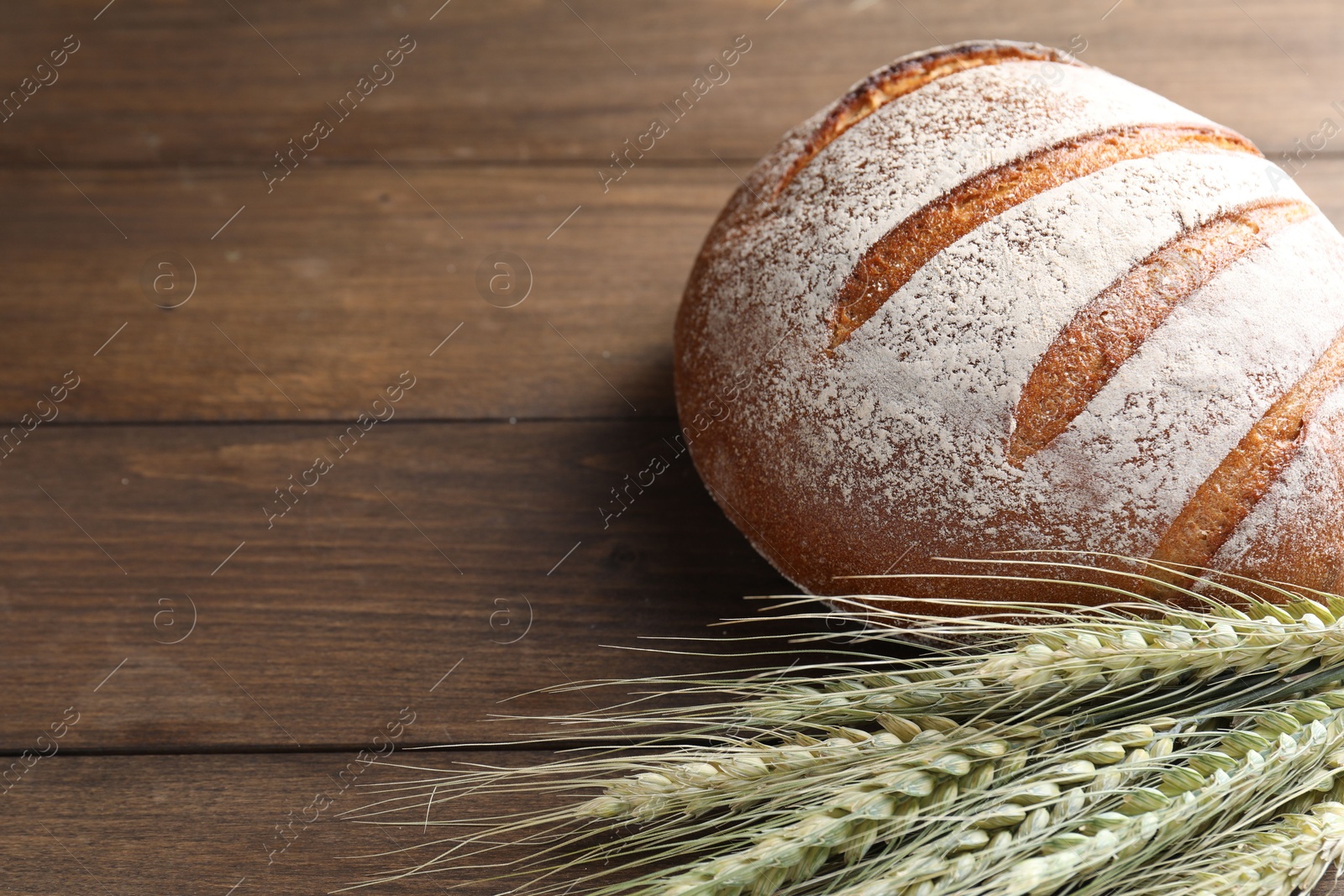 Photo of Fresh bread and green wheat spikes on wooden table, closeup. Space for text