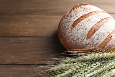 Photo of Fresh bread and green wheat spikes on wooden table, closeup. Space for text