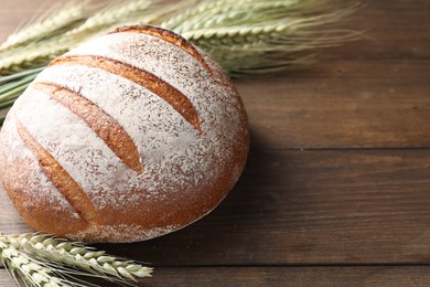 Photo of Fresh bread and green wheat spikes on wooden table, closeup. Space for text