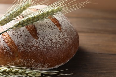 Photo of Fresh bread and green wheat spikes on wooden table, closeup. Space for text