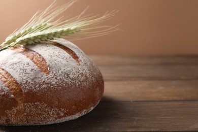 Photo of Fresh bread and green wheat spikes on wooden table, closeup. Space for text