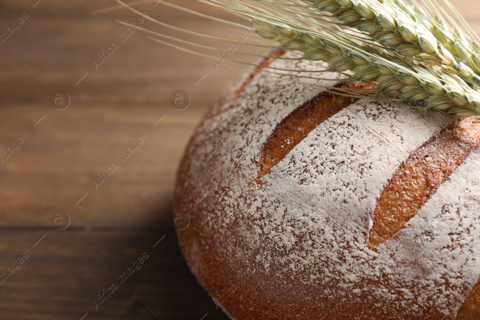 Photo of Fresh bread and green wheat spikes on wooden table, closeup. Space for text