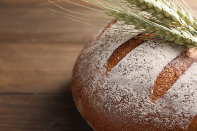 Photo of Fresh bread and green wheat spikes on wooden table, closeup. Space for text