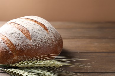 Photo of Fresh bread and green wheat spikes on wooden table, closeup. Space for text