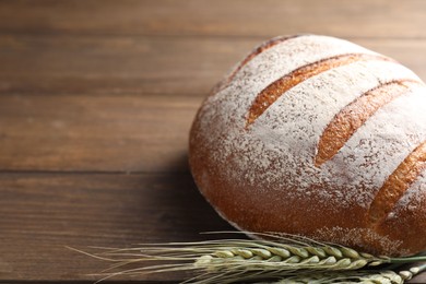 Photo of Fresh bread and green wheat spikes on wooden table, closeup. Space for text
