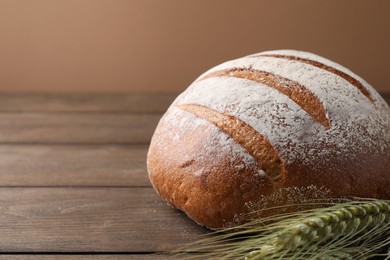 Photo of Fresh bread and green wheat spikes on wooden table, closeup. Space for text