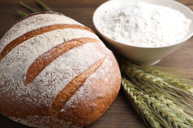 Photo of Fresh bread, flour and green wheat spikes on wooden table, closeup