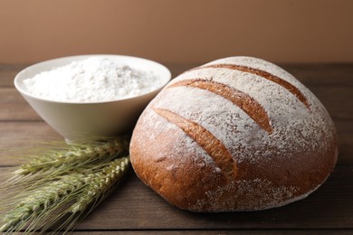 Photo of Fresh bread, flour and green wheat spikes on wooden table, closeup