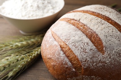 Photo of Fresh bread, flour and green wheat spikes on table, closeup