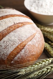Photo of Fresh bread, flour and green wheat spikes on table, closeup