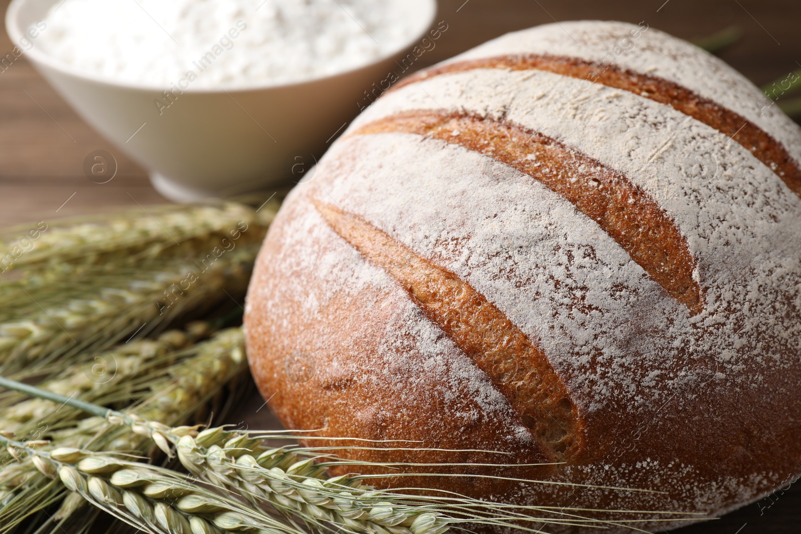 Photo of Fresh bread, flour and green wheat spikes on table, closeup