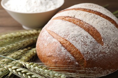 Photo of Fresh bread, flour and green wheat spikes on table, closeup