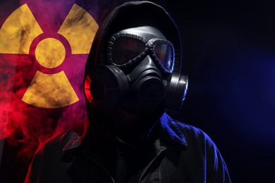 Image of Man wearing gas mask in smoke against black background. Radioactive sign behind him