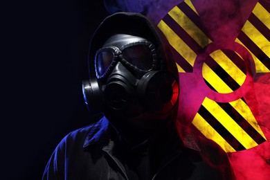 Image of Man wearing gas mask in smoke against black background. Radioactive sign behind him