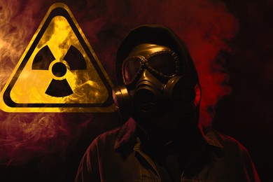 Image of Man wearing gas mask in smoke against black background. Radioactive sign behind him