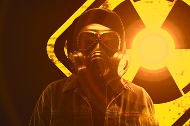 Image of Man wearing gas mask black background. Glowing radioactive sign behind him
