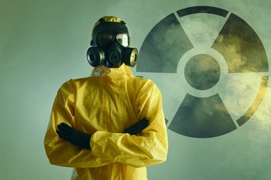 Image of Man wearing hazmat suit and gas mask in smoke. Radioactive sign on color background behind him
