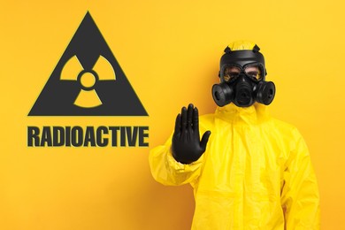 Image of Man in hazmat suit and gas mask showing stop gesture on orange background. Radioactive sign behind him