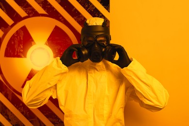 Image of Man wearing hazmat suit and gas mask on orange background. Glowing radioactive sign behind him