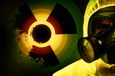 Image of Man wearing hazmat suit and gas mask on dark background. Glowing radioactive sign behind him