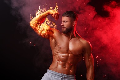 Image of Bodybuilder showing his biceps in smoke against dark background. Muscular man with flaming arm