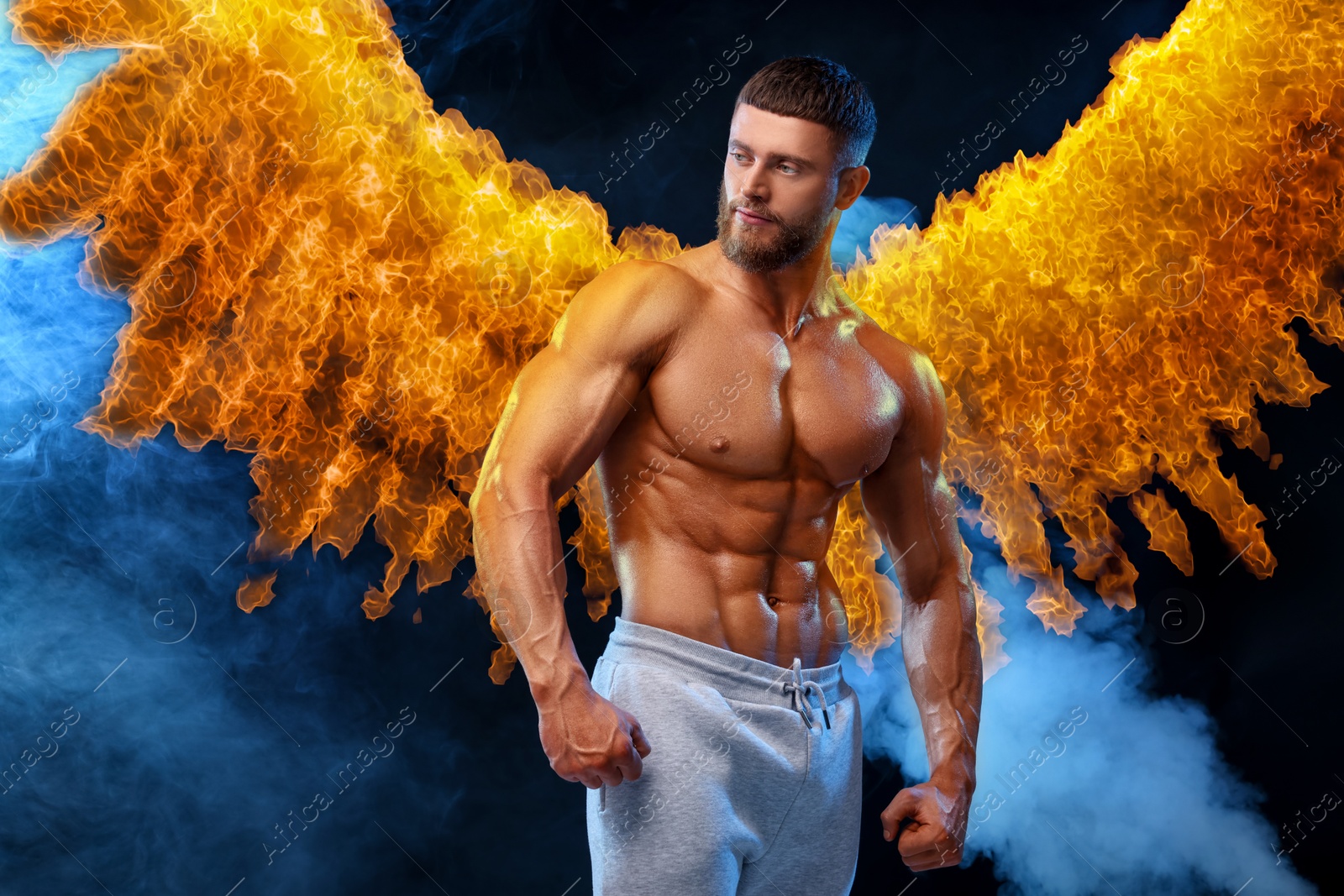 Image of Bodybuilder with flaming wings behind his back against dark background. Shirtless muscular man in smoke