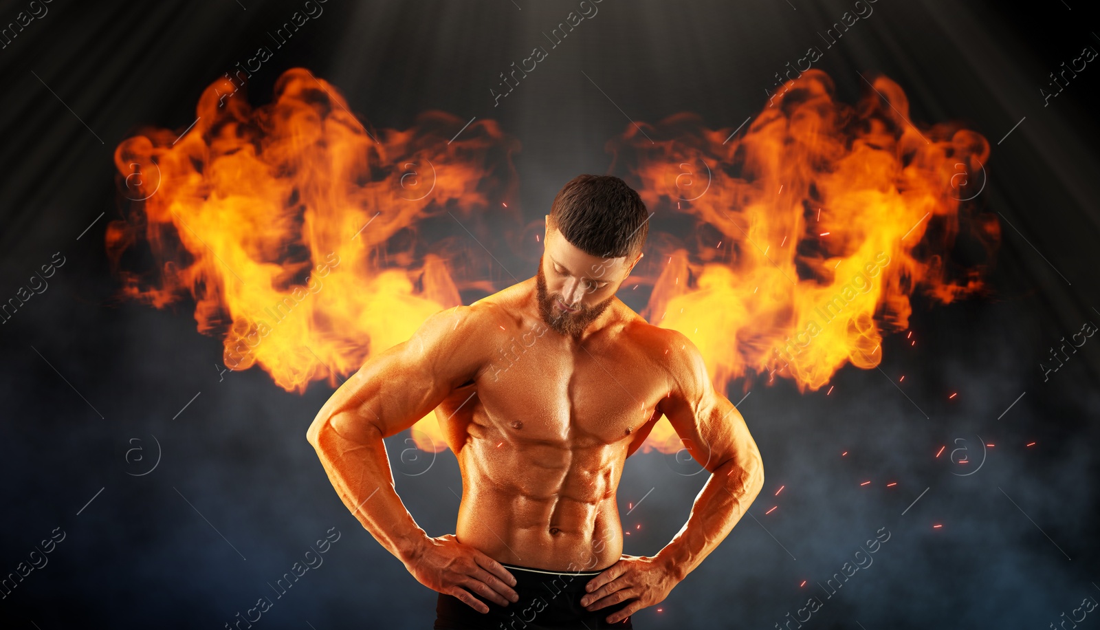 Image of Bodybuilder with flaming wings behind his back against dark background. Shirtless muscular man in smoke