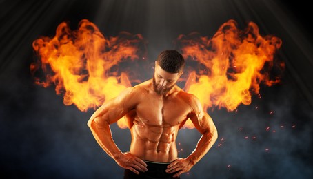 Image of Bodybuilder with flaming wings behind his back against dark background. Shirtless muscular man in smoke